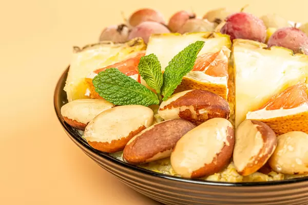 Close-up, porridge with brazil nuts, fruit and mint leaves in a black bowl