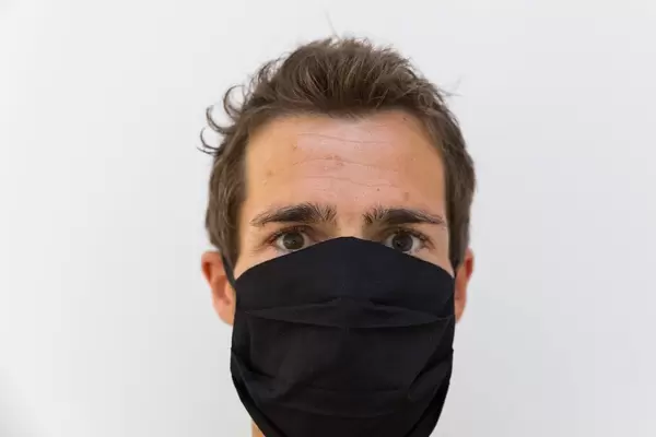 Close-up portrait of a man with a reusable black face mask on a white background