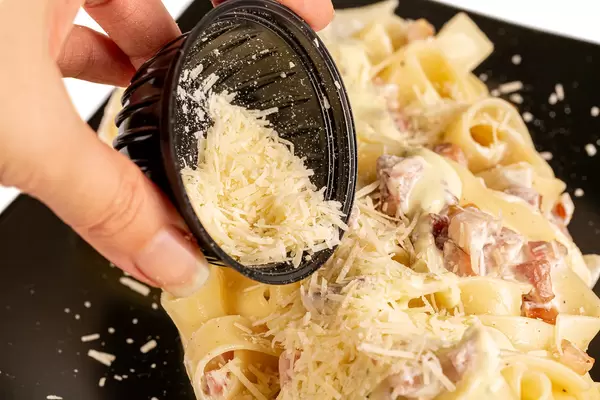 Close-up, pour grated parmesan cheese into carbonara paste