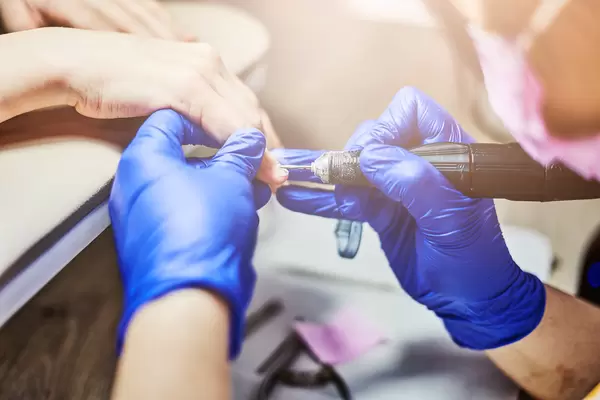 Close-up professional beautician hands working with electric drill file on client fingernails