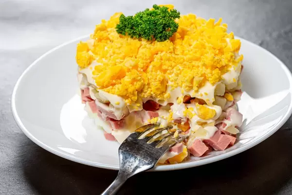 Close-up salad with boiled potatoes, eggs, ham and sauce on a white plate with a fork (Flip 2019)