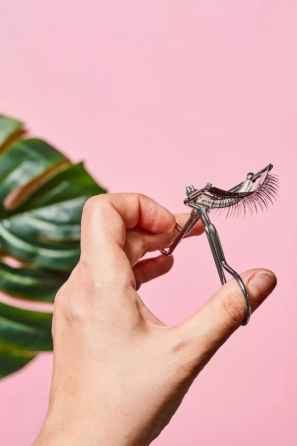 Close-up shot of beauty stylist holding eyelash curler over pink background
