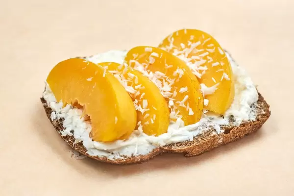 Close-up shot of sour cream spread on toast with peach slices