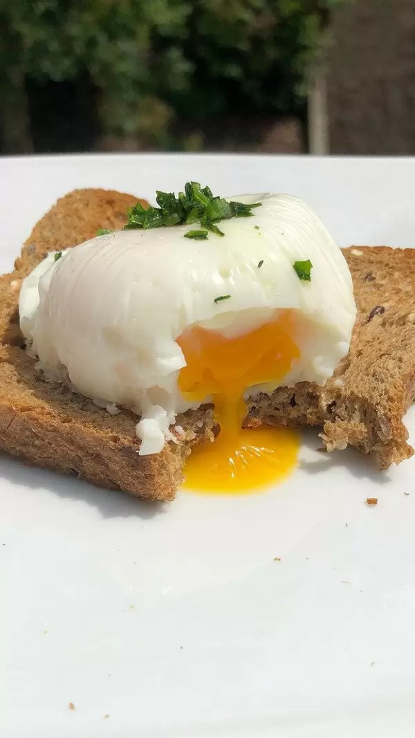 Close-up shows bitten off poached egg on a slice of wholemeal bread with liquid egg yolk, on a white table
