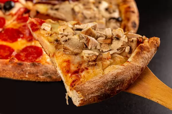 Close-up, slice of pizza with mushrooms and cheese on wooden spatula