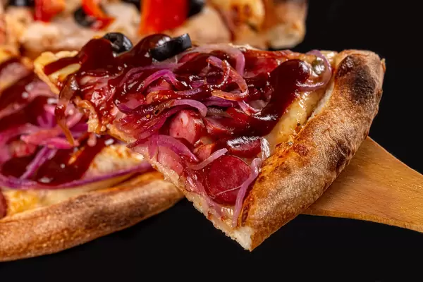 Close-up, slice of pizza with purple onion, smoked sausages and barbecue sauce