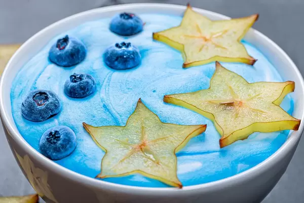 Close up slices of fresh ripe carambola and blueberry berries with blue yogurt on oatmeal