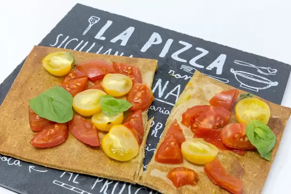 Close Up - The low carb vegan pizza crust made from chia an flaxseeds as a bruschetta topped with fresh cherry tomatoes and basil leaves