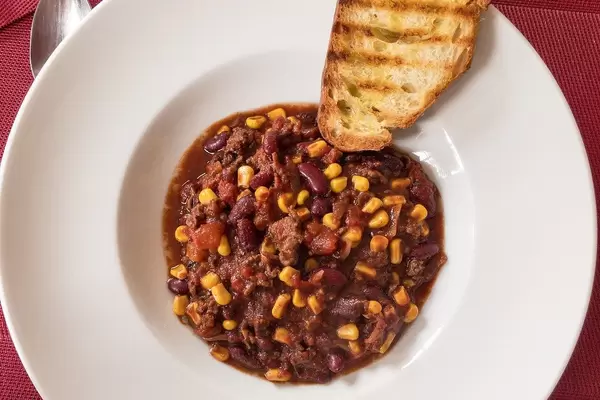 Close Up Top View Food Photo of Chili Con Carne with Ground Pork, Tomatoes, Beans and Corn with Slice of Bread