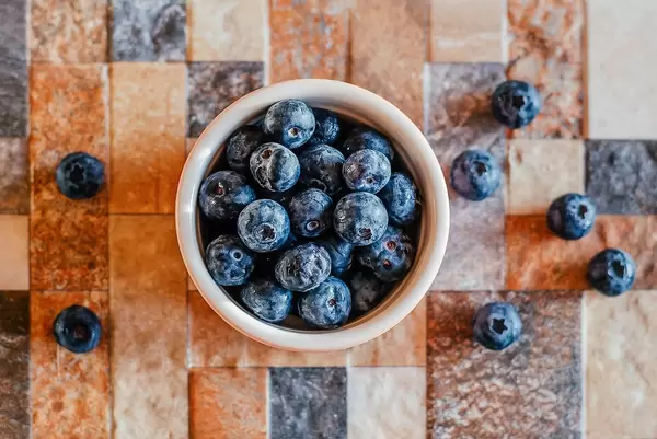 Close Up Top View Photo of Blueberries in Ceramic Bowl on Colorful Tiled Background