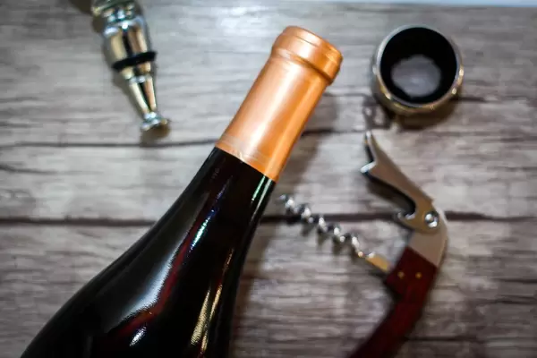 Close Up Top View Photo of Closed Wine Bottle with Corkscrew on Wooden Background