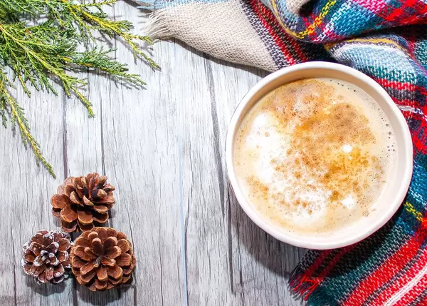 Close Up Top View Photo of Large Coffee Cup next to Scarf and Pinecones on Wooden Background