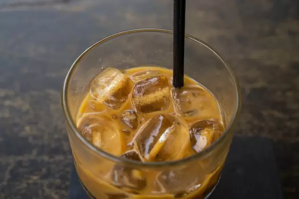 Close Up Top View Photo of Vietnamese Iced Coffee with Sweetened Condensed Milk in a Glass with Plastic Drinking Straw on a Wooden Table