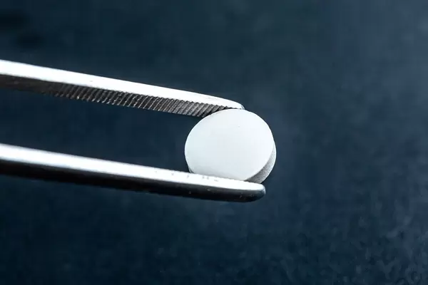 Close-up, tweezers holding a white pill