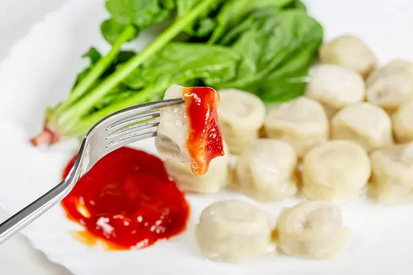 Close up vegetarian dumplings with spinach and tomato sauce on a fork