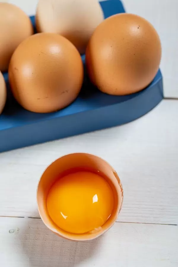 Close-up view of raw chicken eggs in egg box on white wooden background