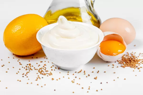 Close-up von hausgemachter Mayonnaise, Olivenöl, Eier, Zitronenon und Senf auf weißem Hintergrund