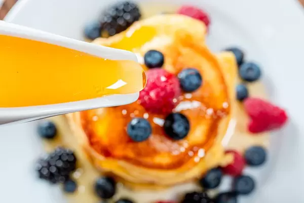 Closeup of honey pouring on the pancakes with berries
