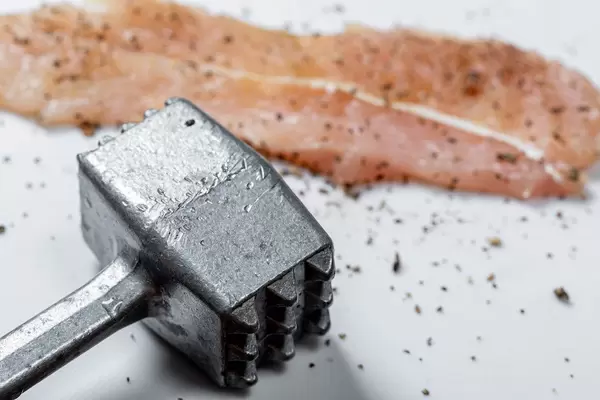 Closeup of iron hammer and a raw chop with spices. The concept of cooking