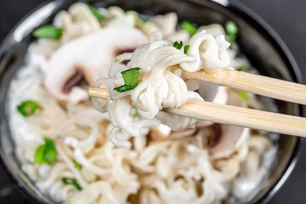 Closeup of pasta with cheese and onion greens on chopsticks