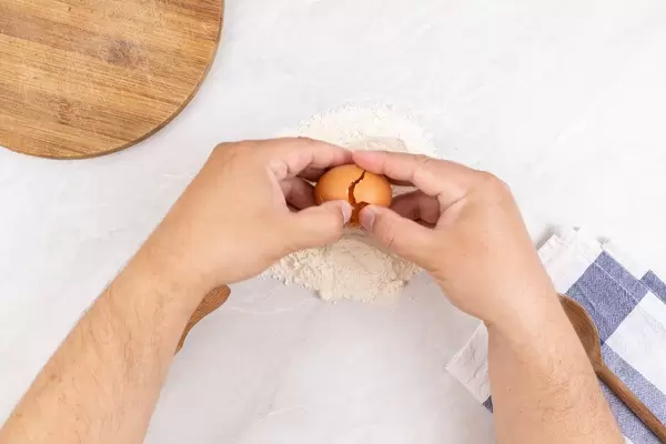 Closeup photo of baker Cracking Egg for dough