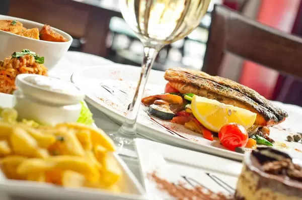 Closeup photograph of different plates of delicious food on a table like fish, fries, vegetables and white wine at a fancy restaurant