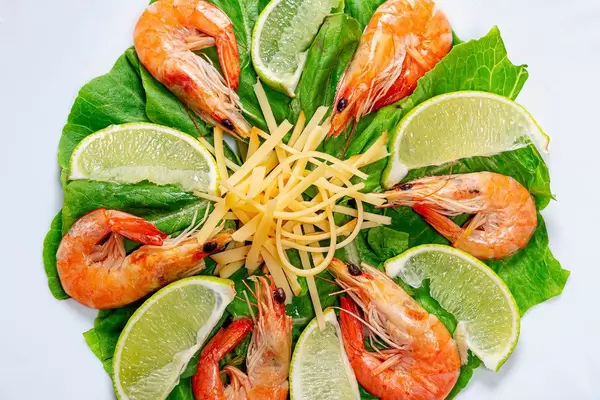 Closeup salad with romaine lettuce, shrimps, lime slices and grated cheese