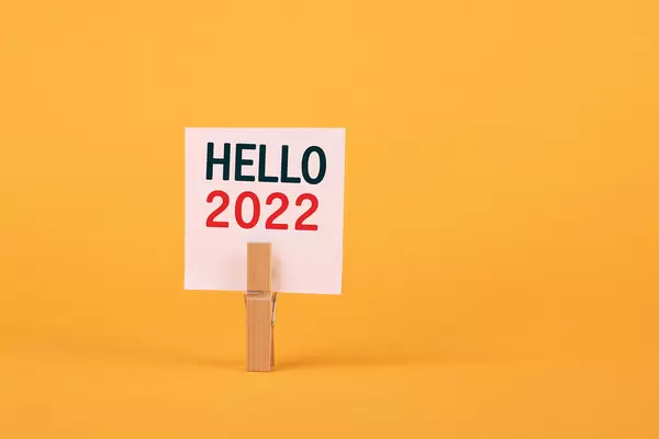 Cloth pin holding peace of paper with Hello 2022 text on yellow background