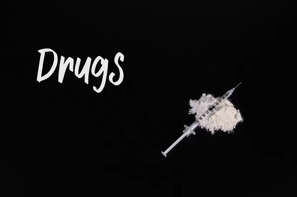 Cocaine powder with syringe and Drugs text on black table