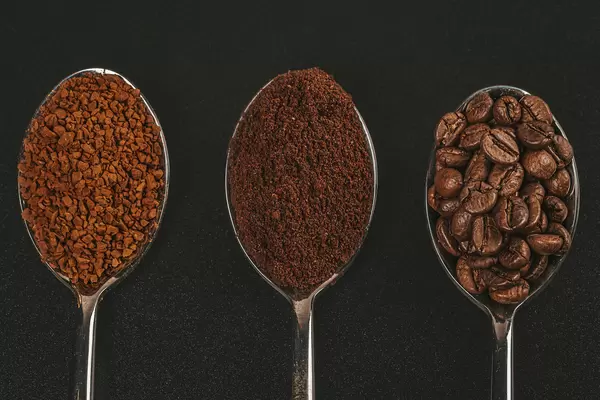 Coffee beans, ground and instant coffee granules in spoons, top view