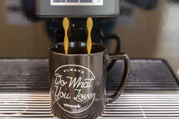 Coffee break at rental office WeWork in Cologne: close-up of a coffee machine pouring a hot drink into a black cup with text "Always do what you love"