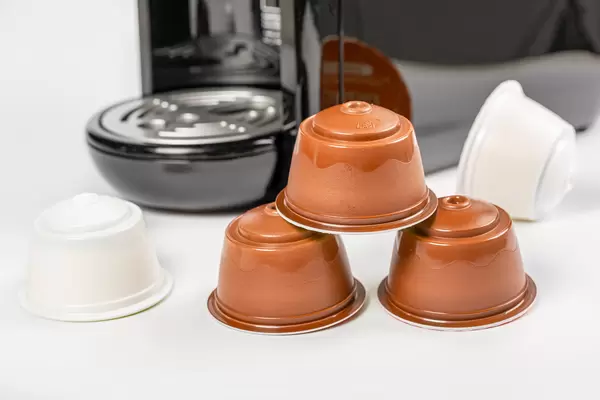 Coffee capsules on white background with coffee maker behind