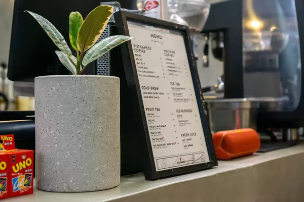 Coffee Shop Menu with many different Drinks next to Plant Pot and Speaker at a Cafe Cash Desk