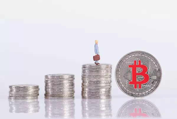 Coin stacks with miniature businessman and silver Bitcoin coin