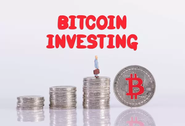 Coin stacks with miniature businessman, silver Bitcoin coin and Bitcoin Investing text