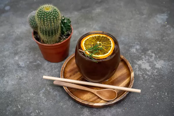 Cold Brew Coffee with Burnt Orange on a Wooden Saucer with Wooden Spoon and Paper Straw next to a Cactus
