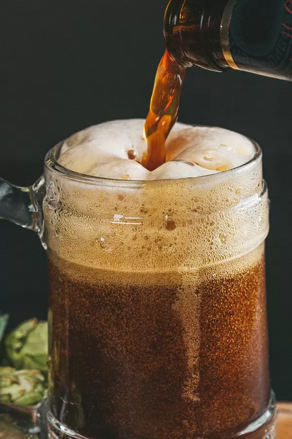Cold dark beer is poured into a beer mug from a bottle