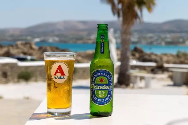 Cold Heineken beer next to a filled glass on a table at a Beach on Paros, with view of the Mediterranean Sean