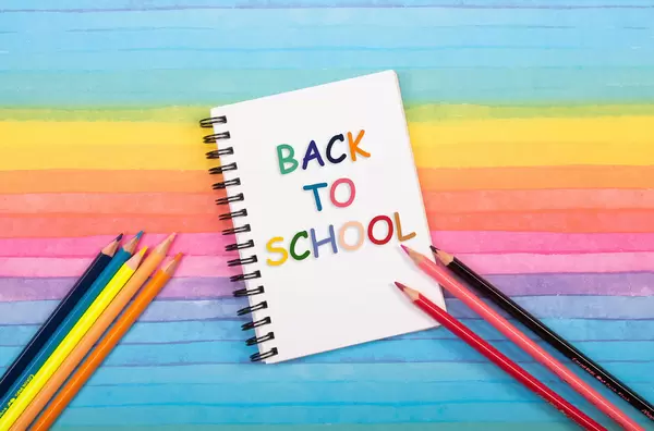 Colored pencils and notebook with back to School text on colorful background