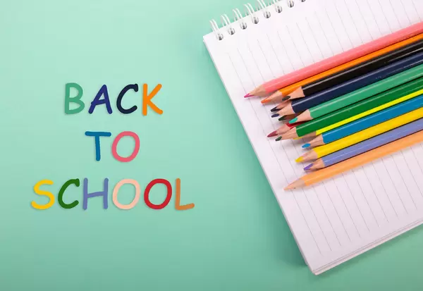 Colored pencils and notebook with Back to School text on green background