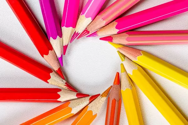 Colored pencils laid out in a circle on a white background