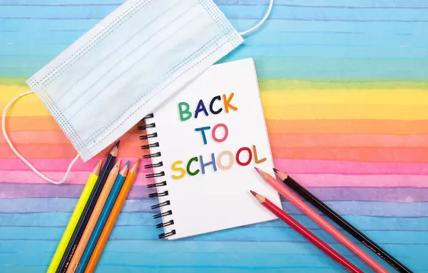 Colored pencils, medical face mask and notebook with back to School text on colorful background