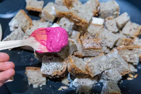 Colorful food: Beetroot hummus on a wooden spoon and pieces of bread in the background
