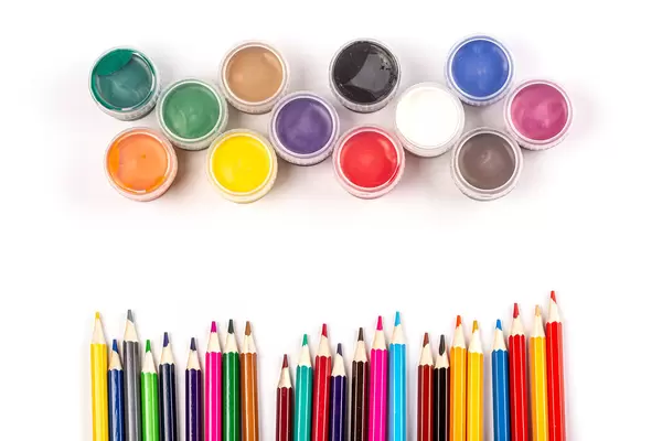 Colorful paints and colored pencils on a white background, top view