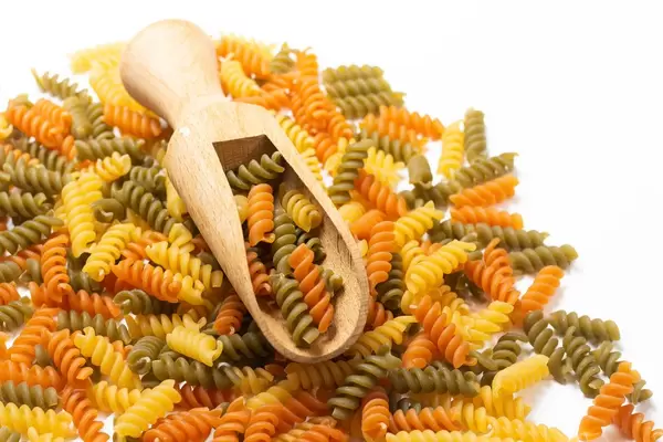 Colorful raw macaroni with wooden spatula on the top