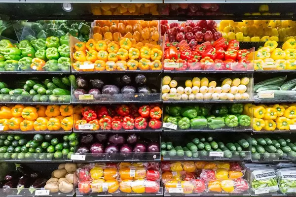 Colorful shelf at organic food supermarket Whole Foods Market, with different vegetables like eggplants, cucumbers, and all sorts of bell pepper