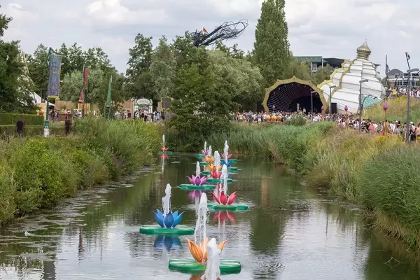 Colorful water lily fountains splashing water in the lake of Tomorrowland festival with partying people in the background