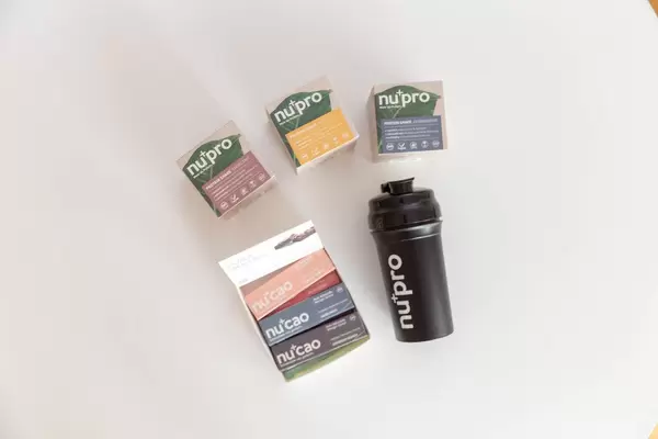 Colourful Nu-Company packaging, with raw cocoa "NuCao", the protein shakes "NuPro" and a black drinking bottle for athletes