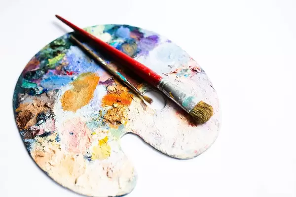 Colourful painter's palette with oil paint and brushes on white background