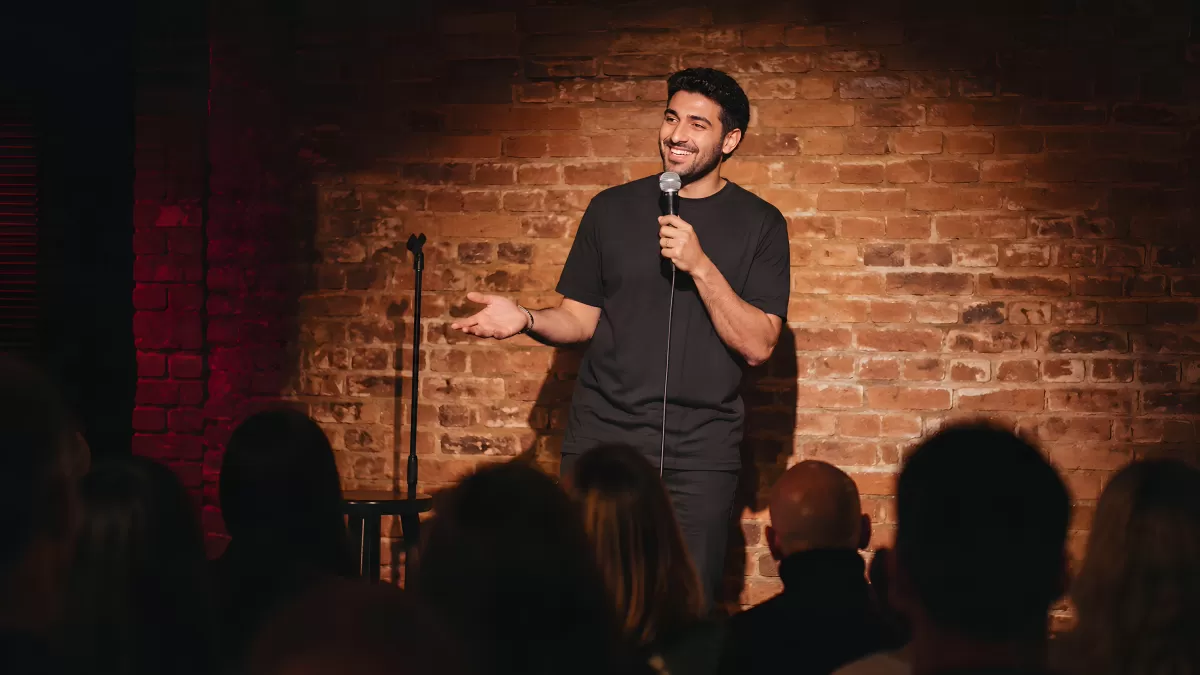Comedian auf Bühne mit Mikrofon vor Backsteinwand